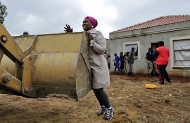 An unidentified woman unsuccessfully tries to stop a bulldozer from demolishing her home in Lenasia.
